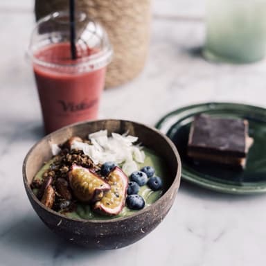 En röd smoothie, en kaka och en skål med frukt.