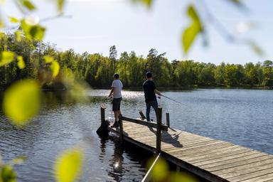 Två killar fiskar på en brygga i en sjö.