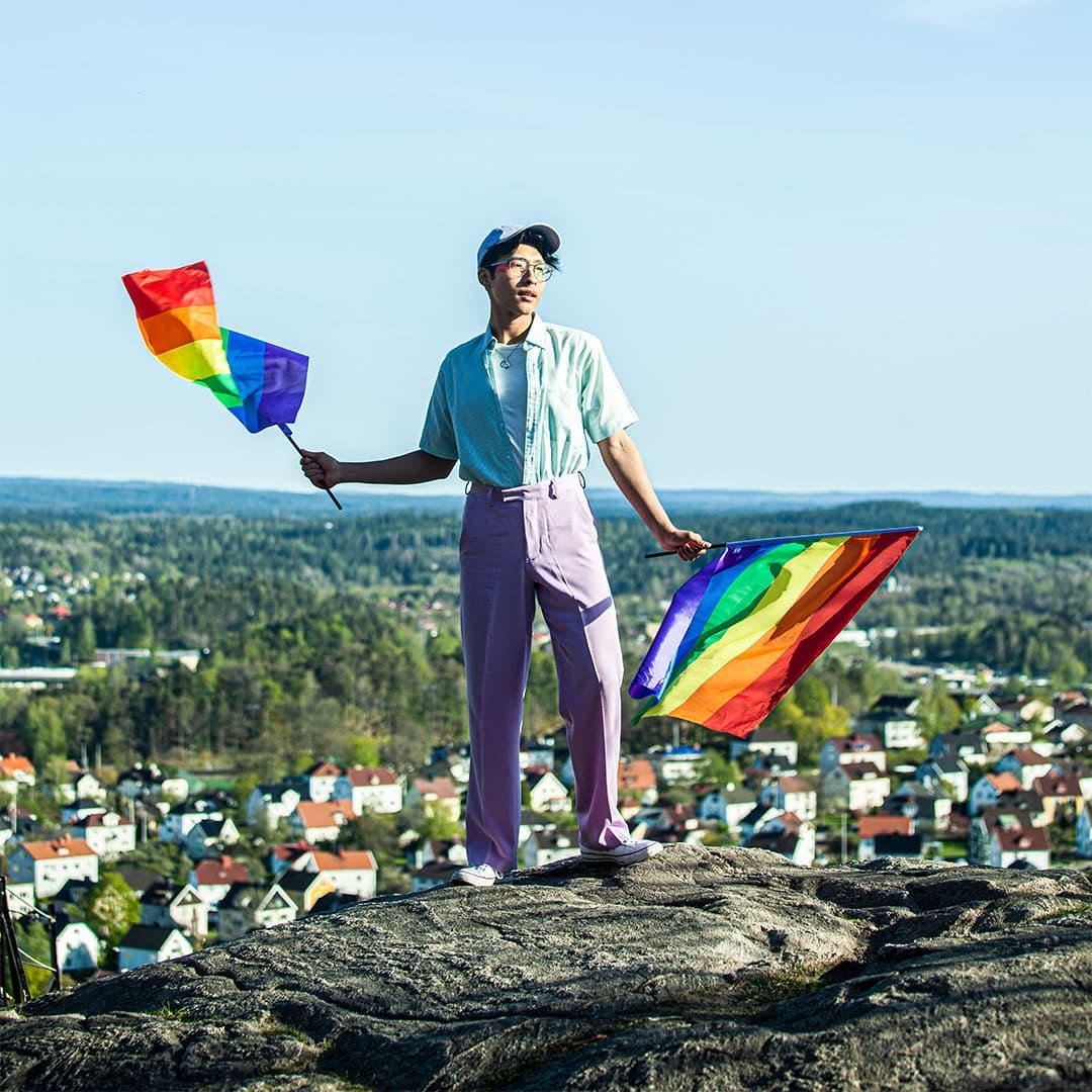 Person som står på ett berg och håller i två prideflaggor