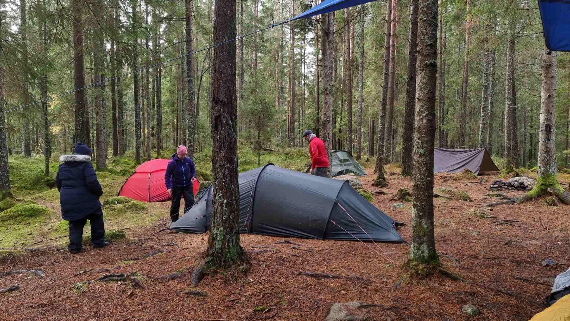 några personer sätter upp tält i skogen det är höst de har varma kläder